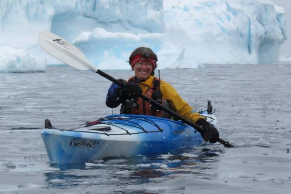 Louise Adie displays a wide grin from her kayak's seat. in front of glaciers.