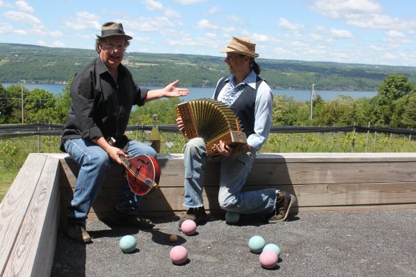 two men in hats sitting on bocce court railing overlooking Seneca Lake looking at one another and the view and smiling