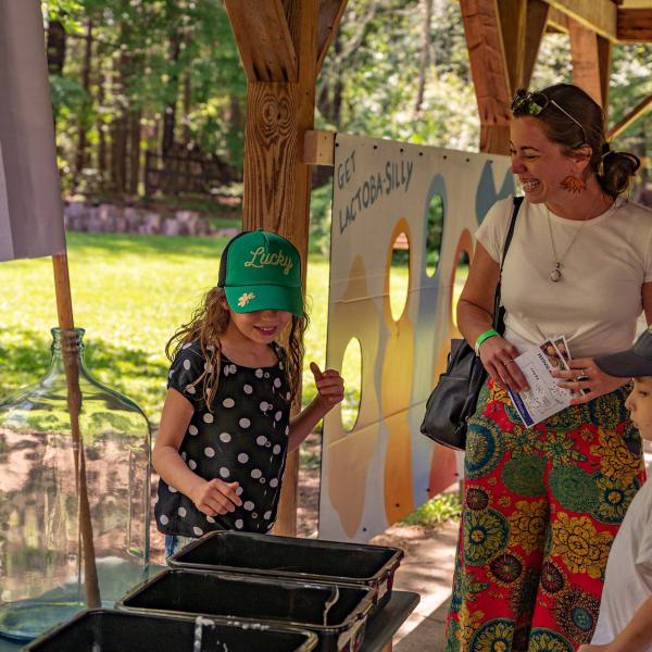 A little girl stands with her family at the Fermentation Petting Zoo, seeing what tempeh feels like!
